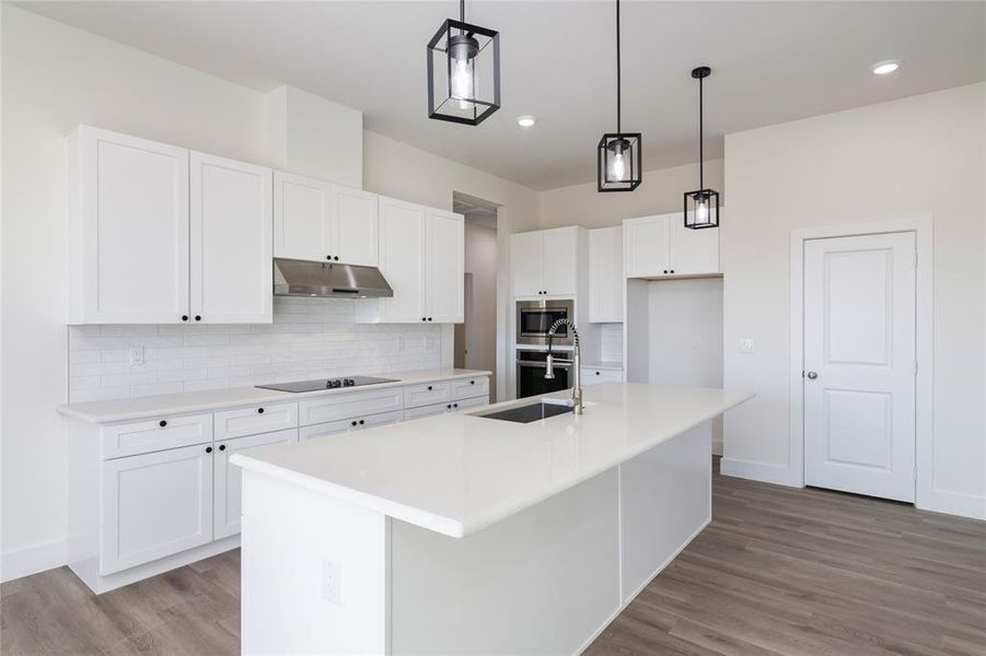 Kitchen with appliances with stainless steel finishes, a kitchen island with sink, decorative light fixtures, light hardwood / wood-style floors, and white cabinetry