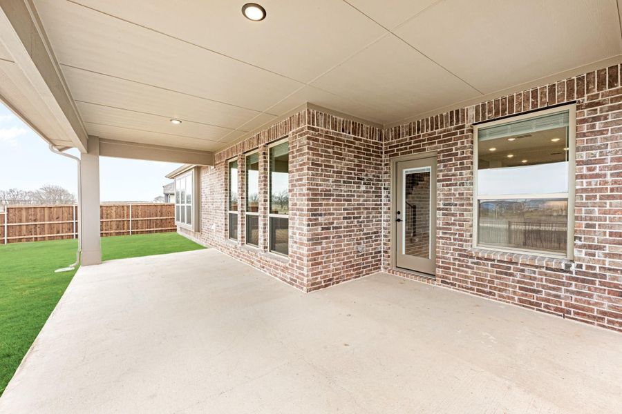 Covered concrete patio with brick exterior, back door, and fenced yard with green lawn Covered concrete patio with brick exterior, back door, and fenced yard with green lawn