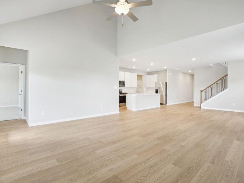 Unfurnished living room featuring ceiling fan, a high ceiling, baseboards, light wood finished floors, and stairs Unfurnished living room featuring ceiling fan, a high ceiling, baseboards, light wood finished floors, and stairs