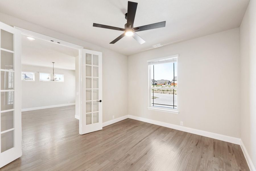 Empty room with hardwood floors, ceiling fan, and French doors leading to adjacent space