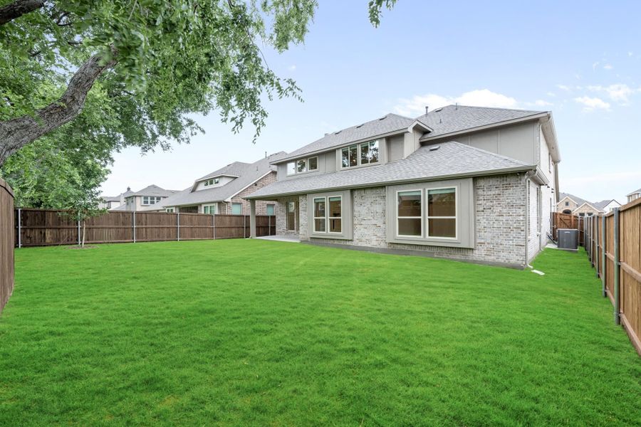 Backyard of two-story brick home with large green lawn and wood privacy fence Backyard of two-story brick home with large green lawn and wood privacy fence