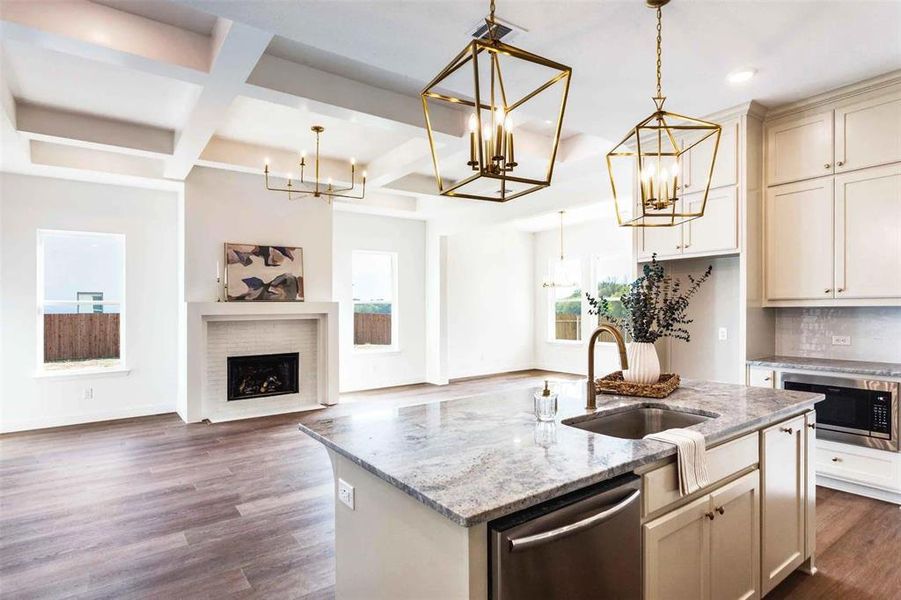 Kitchen with light stone countertops, a kitchen island with sink, cream cabinets, open floor plan, and coffered ceiling