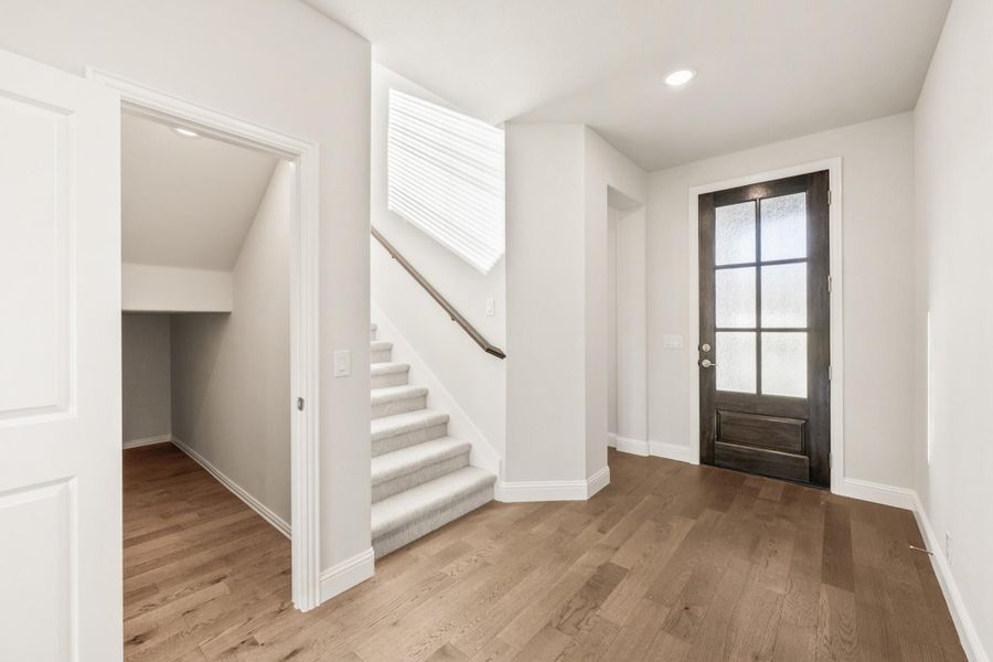 Entryway with dark wood front door, carpeted staircase, and hardwood floors with under-stair storage