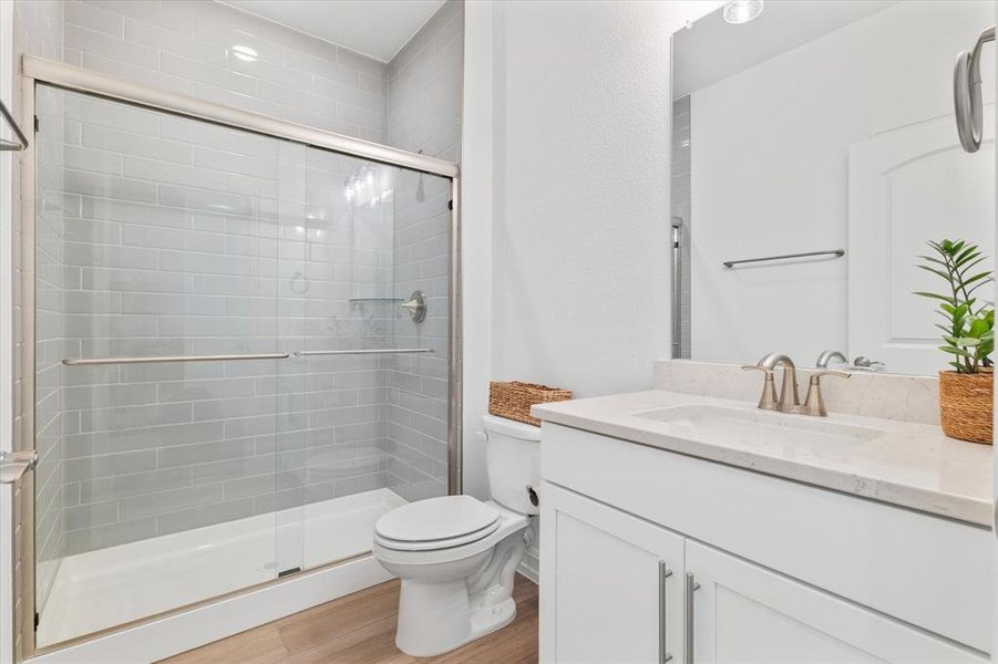 Bathroom featuring a glass-enclosed shower with subway tile surround, a white vanity with integrated sink, a full-width mirror, and wood-finish flooring