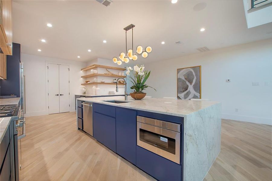 Kitchen featuring sink, stainless steel appliances, light stone counters, light hardwood / wood-style flooring, and an island with sink