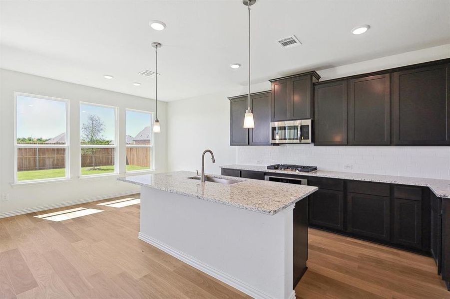 Kitchen featuring light wood-type flooring, appliances with stainless steel finishes, hanging light fixtures, and sink