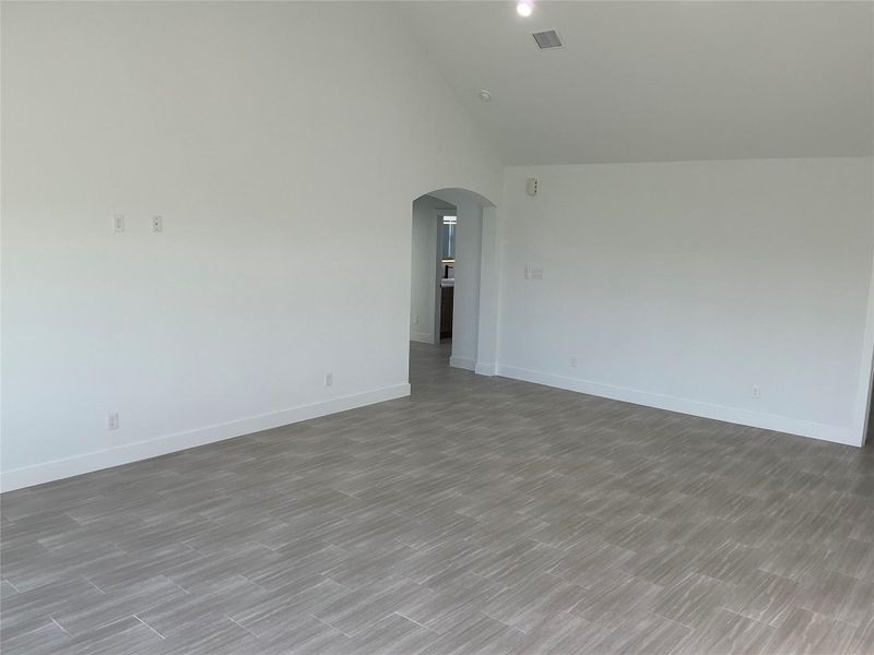 This photo features a spacious room with light gray tile flooring and white walls, offering a clean, modern look. The arched doorway leads to another area, enhancing the open layout.