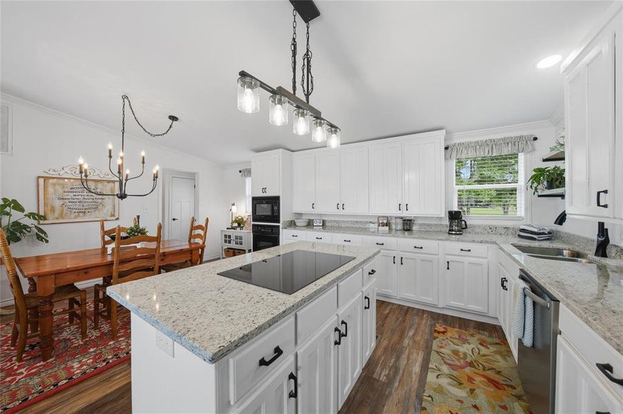 Modern kitchen featuring white cabinetry, granite countertops, an island with an integrated cooktop, stainless steel appliances, and wood-finish flooring