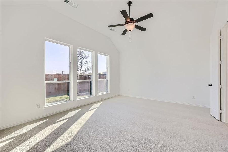 Unfurnished room featuring ceiling fan, light colored carpet, vaulted ceiling, and a wealth of natural light