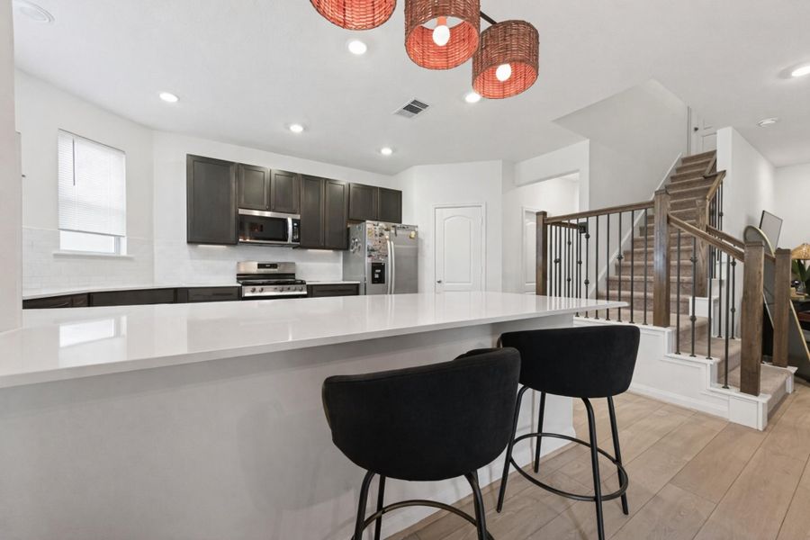 Sleek U-shaped kitchen showcases expansive quartz counters, dark cabinetry, and bright recessed lighting throughout.