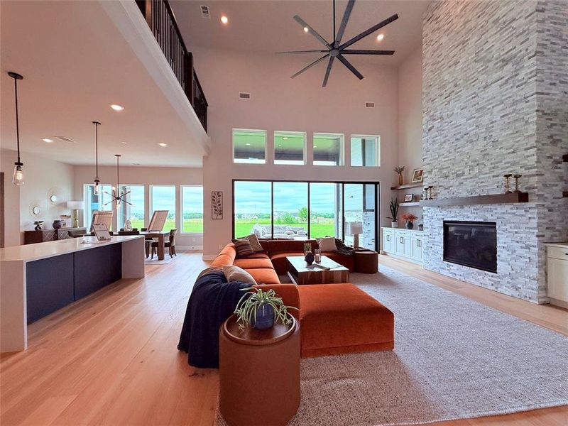 Open-concept living space featuring high ceilings, a stacked stone fireplace with a substantial hearth, and light wood-finish flooring