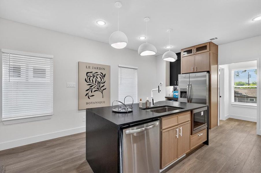 Kitchen featuring a black countertop island with integrated sink, stainless steel dishwasher, and built-in microwave