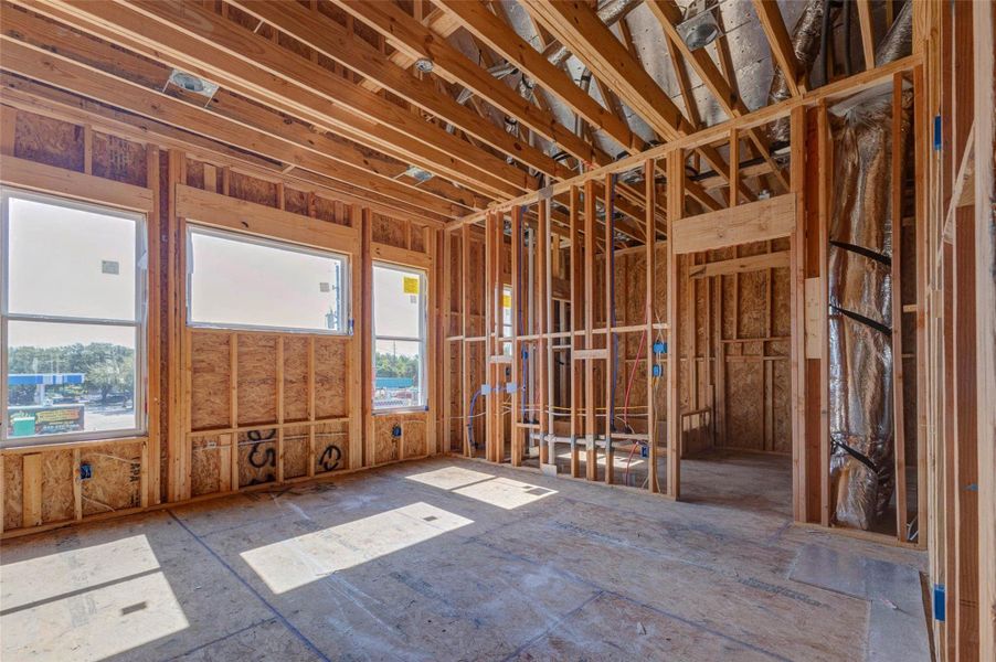 Spacious framed room with large windows, vaulted ceiling lines, and visible HVAC and electrical systems overhead. This construction-stage view highlights the scale, light, and future livability of the space, offering a strong sense of how the finished room will feel once drywall, flooring, and finishes are complete. Spacious framed room with large windows, vaulted ceiling lines, and visible HVAC and electrical systems overhead. This construction-stage view highlights the scale, light, and future livability of the space, offering a strong sense of how the finished room will feel once drywall, flooring, and finishes are complete.