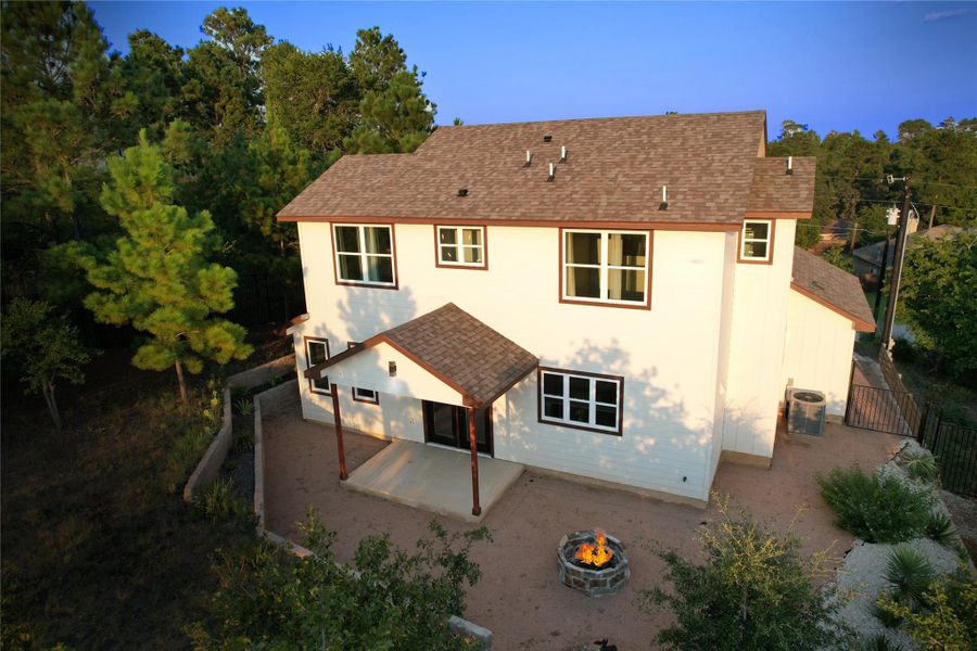 Rear view of house featuring a shingled roof, a patio area, and a fire pit
