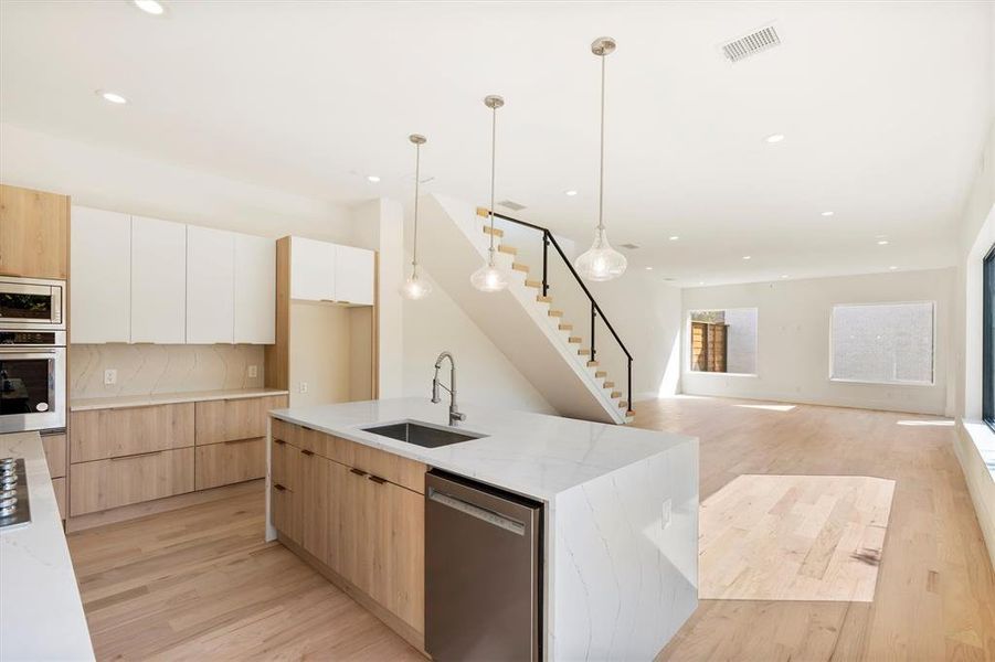 Kitchen with pendant lighting, sink, white cabinetry, stainless steel appliances, and light wood-type flooring