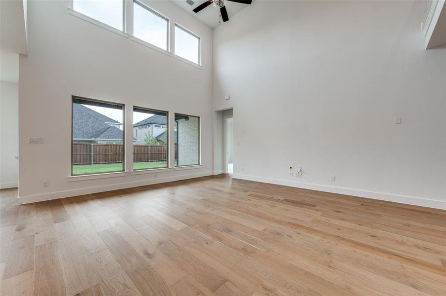 Unfurnished living room featuring ceiling fan, a towering ceiling, and light hardwood / wood-style flooring