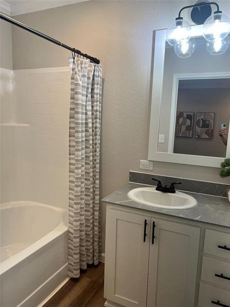 Bathroom with vanity, shower / tub combo, dark wood-style floors, and a textured wall