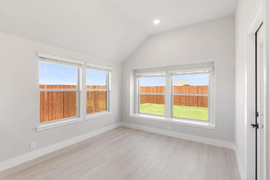 Empty bedroom with vaulted ceiling, light wood floors, and four windows overlooking a fenced backyard Empty bedroom with vaulted ceiling, light wood floors, and four windows overlooking a fenced backyard
