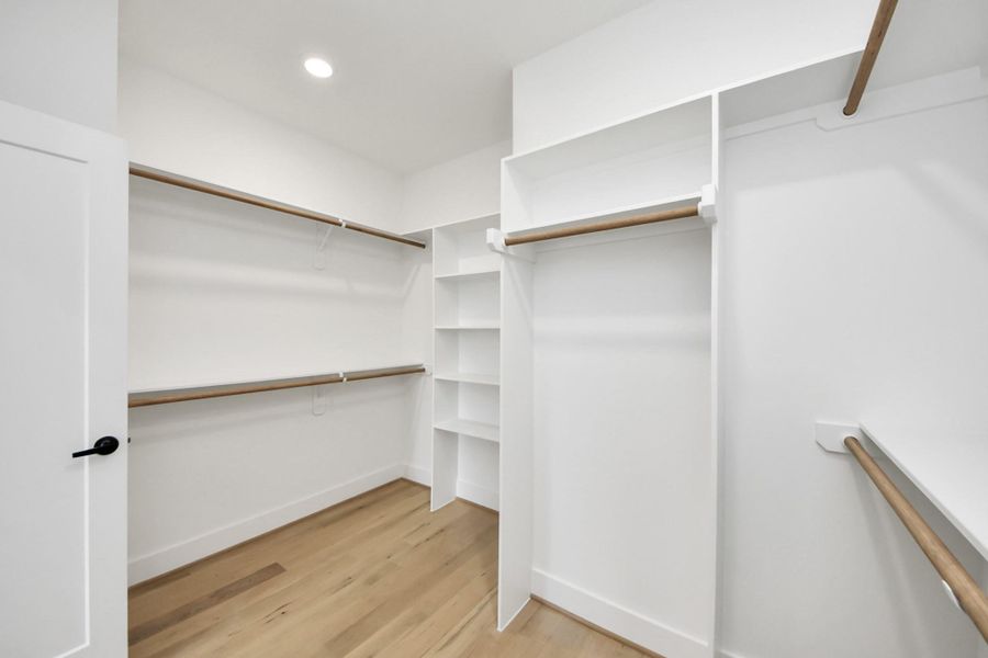 Spacious walk-in closet with built-in shelving, plenty of hanging space, and hardwood flooring. Bright and well-lit, ideal for organization and storage.