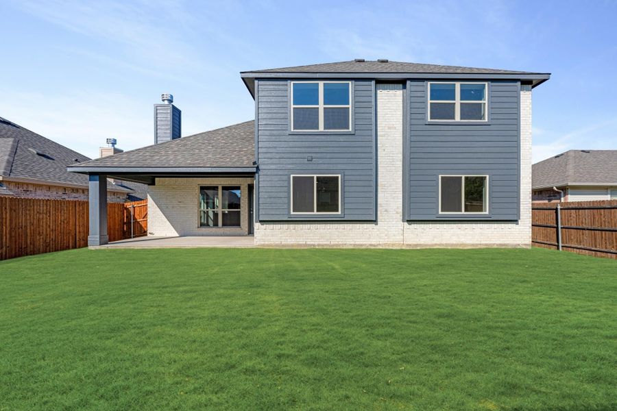 Two-story home rear exterior with gray siding, brick accents, covered patio, and fenced backyard with green lawn Two-story home rear exterior with gray siding, brick accents, covered patio, and fenced backyard with green lawn
