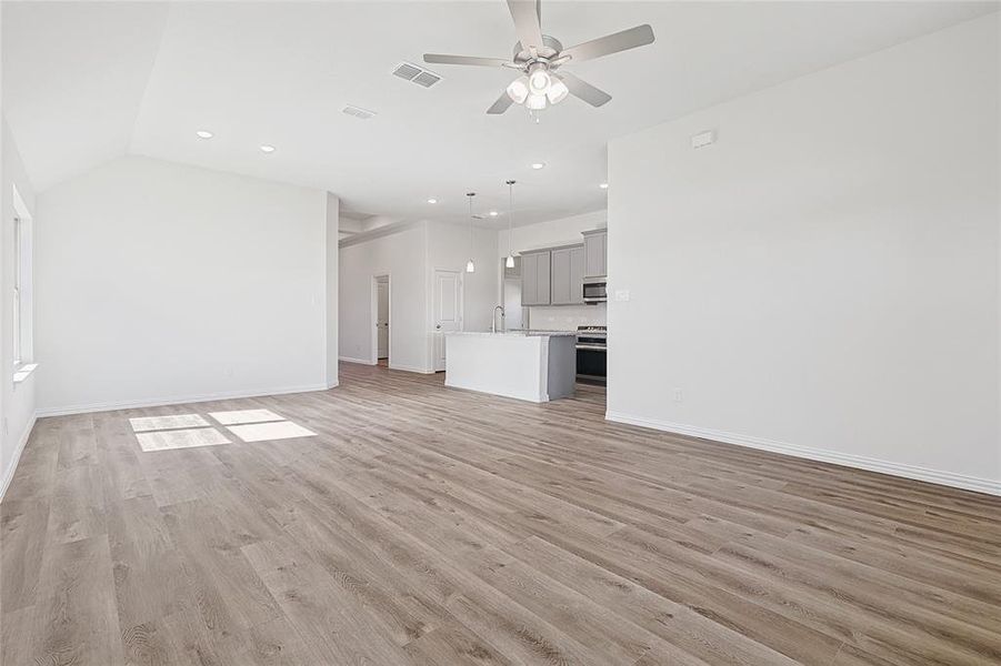 Unfurnished living room with light wood-type flooring, ceiling fan, and lofted ceiling