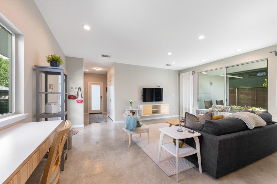 Concrete floors ground this living space, featuring high ceilings and sliding glass doors to the outside. Concrete floors ground this living space, featuring high ceilings and sliding glass doors to the outside.