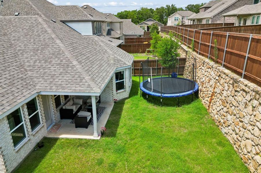 Expansive backyard with a manicured lawn, stone retaining wall, and a wood privacy fence