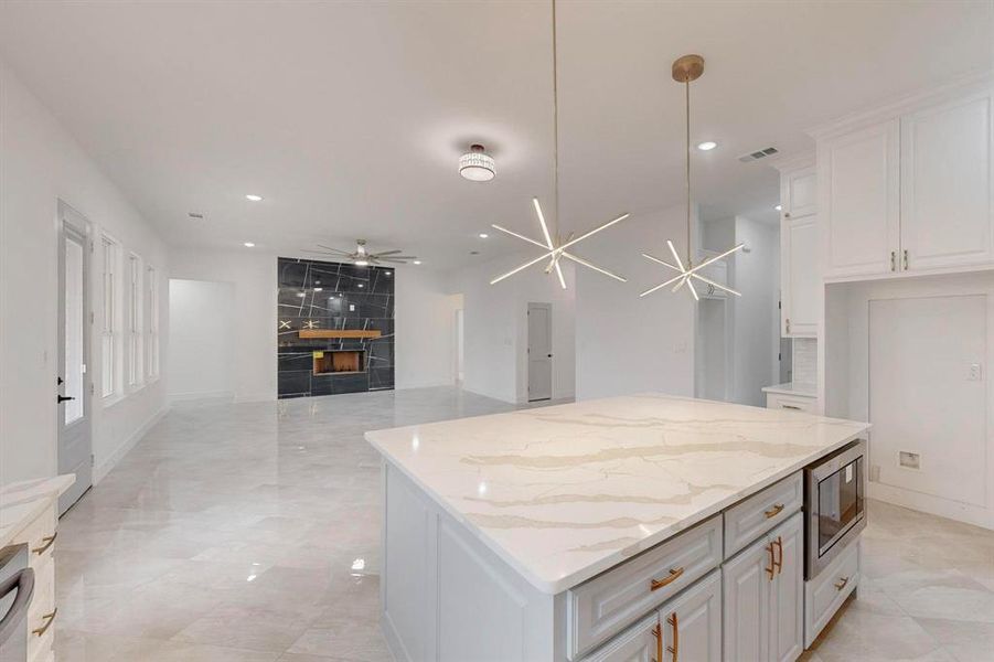 Kitchen featuring white cabinets, a center island, light stone countertops, open floor plan, and stainless steel microwave