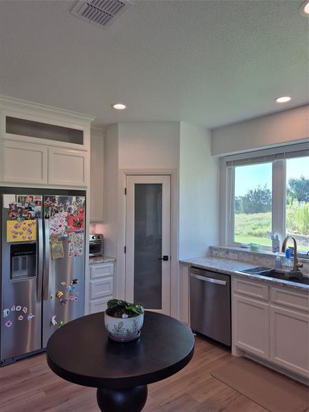 Kitchen featuring white cabinets, refrigerator, light wood-type flooring, stainless steel dishwasher, and light stone counters