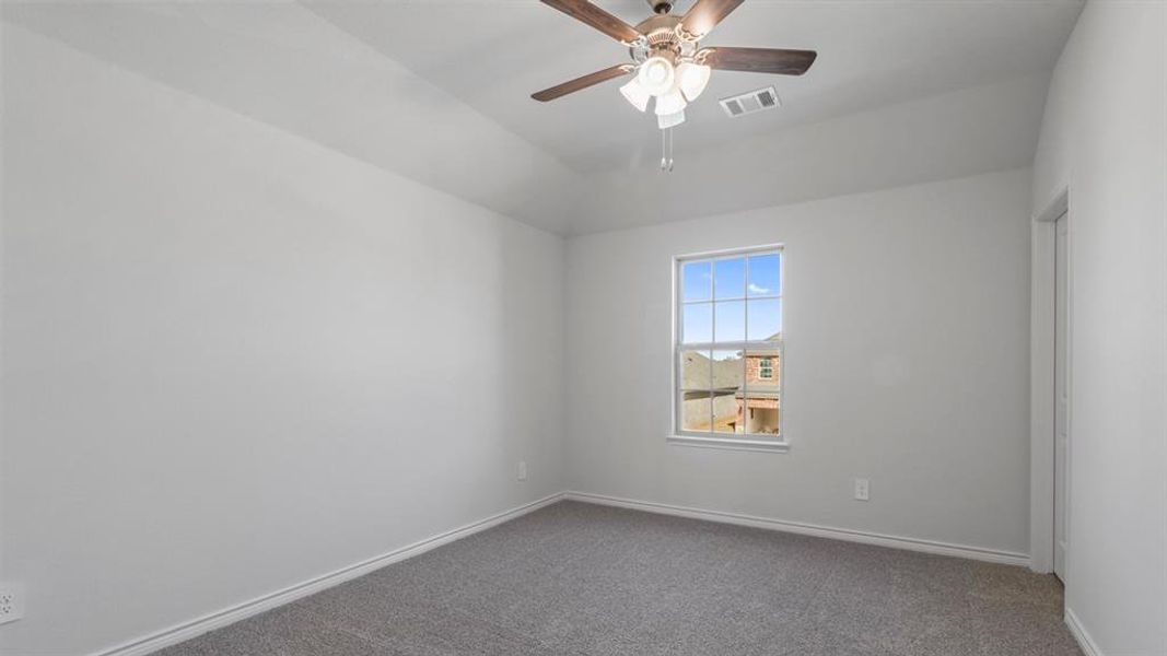 Carpeted spare room featuring vaulted ceiling and a ceiling fan