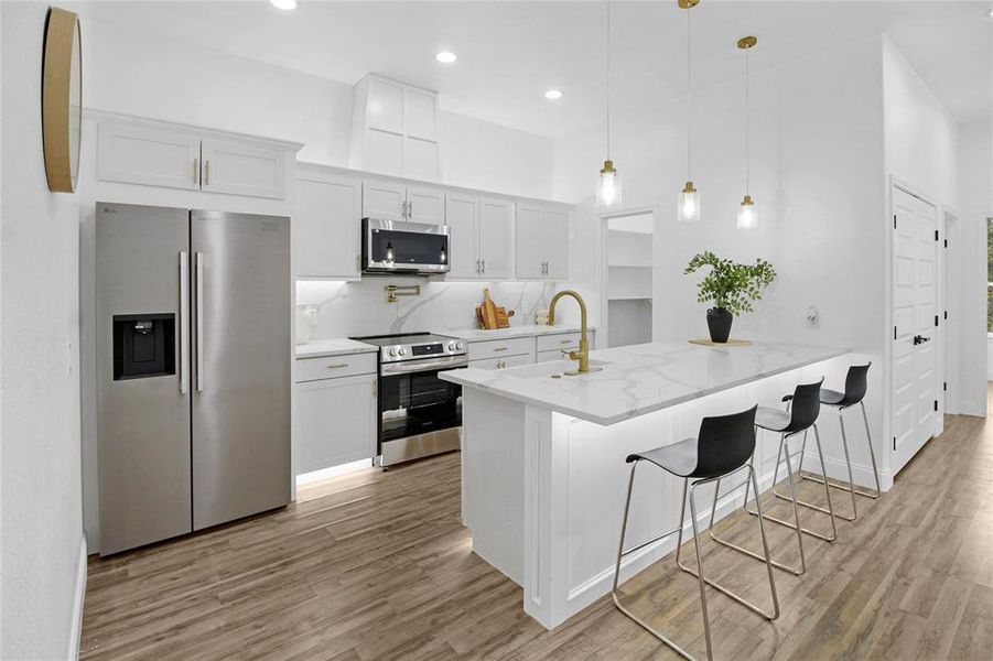 Kitchen with appliances with stainless steel finishes, white cabinetry, a breakfast bar, a towering ceiling, and recessed lighting Kitchen with appliances with stainless steel finishes, white cabinetry, a breakfast bar, a towering ceiling, and recessed lighting