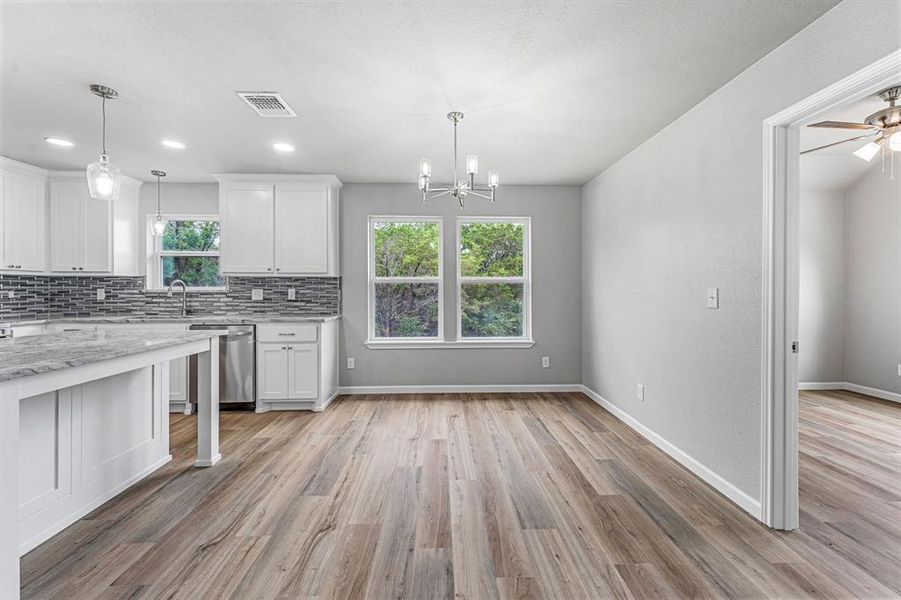 Kitchen with stainless steel dishwasher, white cabinets, a chandelier, tasteful backsplash, and light wood-type flooring Kitchen with stainless steel dishwasher, white cabinets, a chandelier, tasteful backsplash, and light wood-type flooring