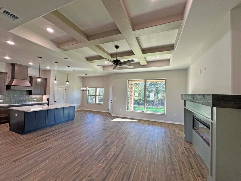 Kitchen featuring coffered ceiling, a glass covered fireplace, dark wood-style flooring, open floor plan, and hanging light fixtures Kitchen featuring coffered ceiling, a glass covered fireplace, dark wood-style flooring, open floor plan, and hanging light fixtures