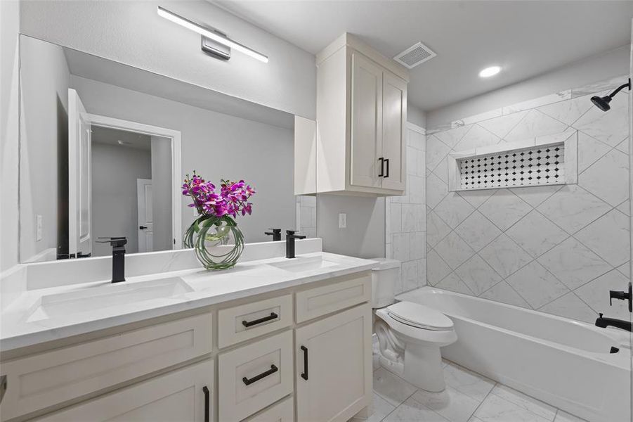 Bathroom featuring a double vanity with matte black fixtures, an expansive mirror with integrated lighting, a white bathtub, and a tiled shower surround with a decorative niche Bathroom featuring a double vanity with matte black fixtures, an expansive mirror with integrated lighting, a white bathtub, and a tiled shower surround with a decorative niche
