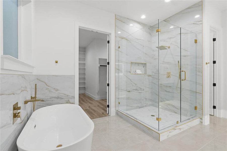 Bathroom featuring a marble finish shower, a walk in closet, a soaking tub, tile walls, and recessed lighting