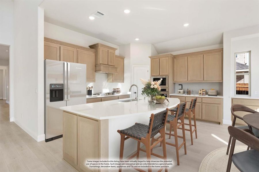 Kitchen with light wood cabinets, center island with seating, and stainless steel refrigerator