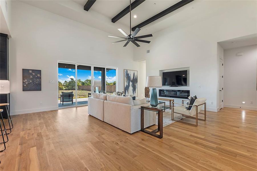 Spacious living area featuring high vaulted ceilings with exposed beams, wood-finish flooring, a built-in media center with an integrated fireplace, and a large sliding glass door opening to the exterior Spacious living area featuring high vaulted ceilings with exposed beams, wood-finish flooring, a built-in media center with an integrated fireplace, and a large sliding glass door opening to the exterior