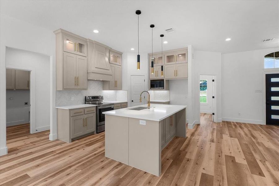 Kitchen with stainless steel appliances, sink, pendant lighting, a center island with sink, and light hardwood / wood-style flooring