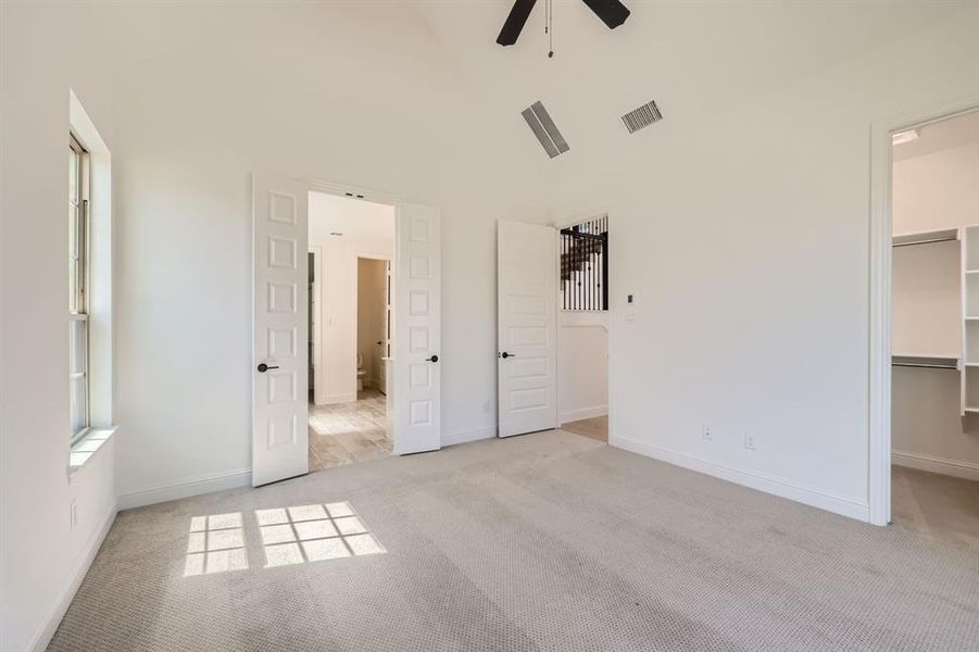 Primary bedroom with ceiling fan, light colored carpet, high vaulted ceiling, a walk in closet, and a closet