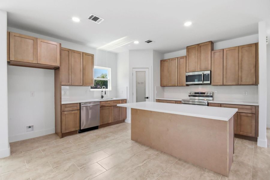 Spacious kitchen featuring modern stainless steel appliances, elegant cabinetry, and a sleek central island, perfect for culinary endeavors and entertaining.