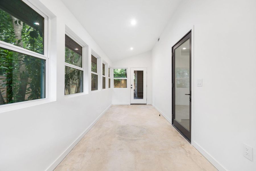 Hallway with unfinished concrete floors, lofted ceiling, and recessed lighting