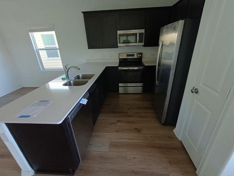 Kitchen with stainless steel appliances, light wood-style floors, dark cabinetry, and a peninsula Kitchen with stainless steel appliances, light wood-style floors, dark cabinetry, and a peninsula