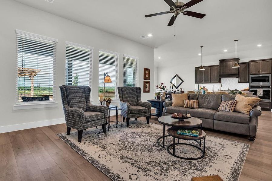 Open-concept living space featuring ceiling fan, ample natural light from multiple windows, an inset electric fireplace, and wood-finish flooring