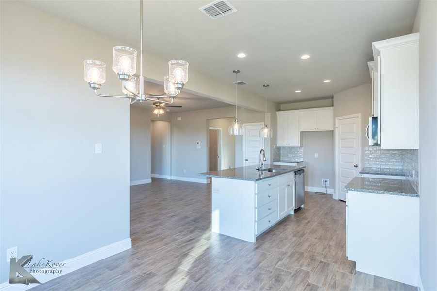 Kitchen featuring dark stone countertops, a chandelier, decorative light fixtures, white cabinets, and backsplash