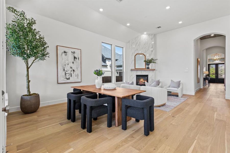 Dining area with arched walkways, light wood-type flooring, recessed lighting, a fireplace, and french doors