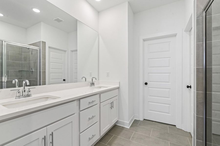 Bathroom featuring a dual vanity with white cabinetry, polished chrome fixtures, and a spacious glass-enclosed shower with gray tiled walls
