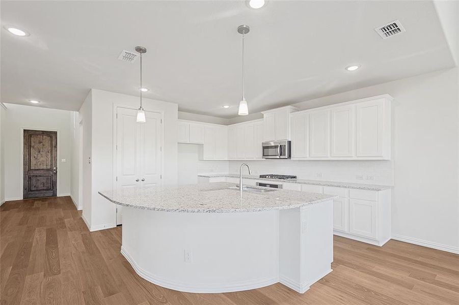 Kitchen featuring light stone countertops, white cabinetry, an island with sink, light wood-type flooring, and stainless steel appliances Kitchen featuring light stone countertops, white cabinetry, an island with sink, light wood-type flooring, and stainless steel appliances