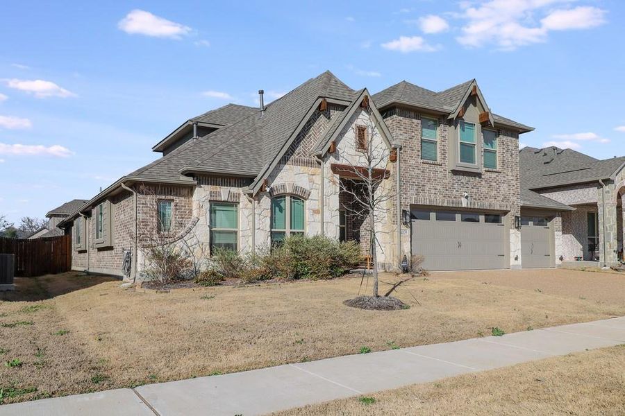 View of front of property featuring an attached garage, brick siding, stone siding, roof with shingles, and a front lawn