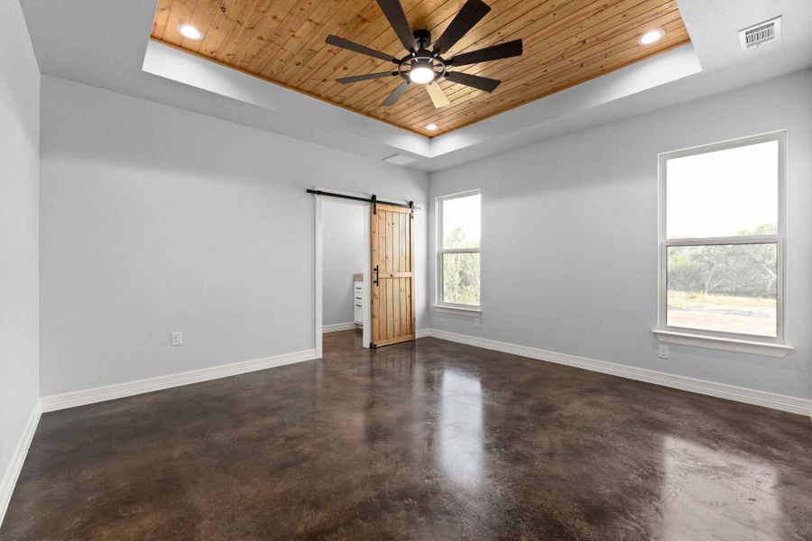 Unfurnished bedroom featuring a raised ceiling, wooden ceiling, a barn door, finished concrete flooring, and recessed lighting