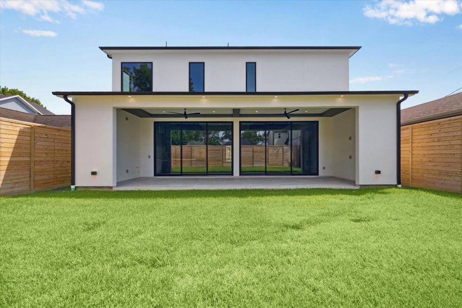 The back view of the home is both striking and inviting, showcasing clean modern architecture framed by sleek lines and expansive glass doors that blend indoor and outdoor living.